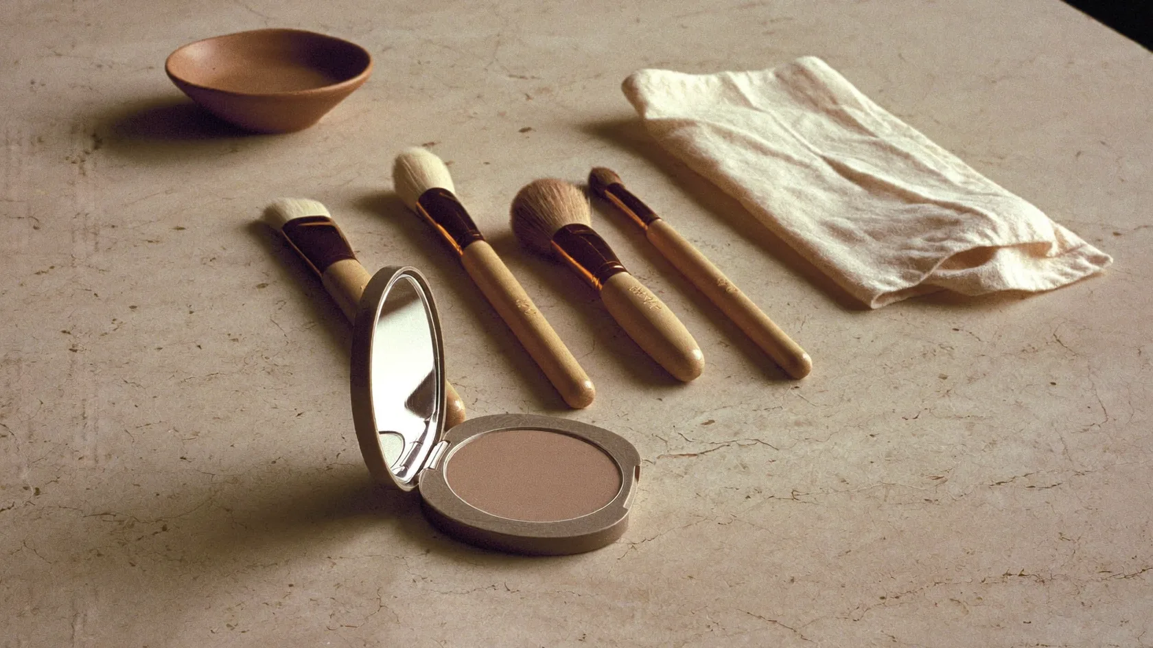 Pinceaux de maquillage et poudre teinte neutre sur une pierre claire