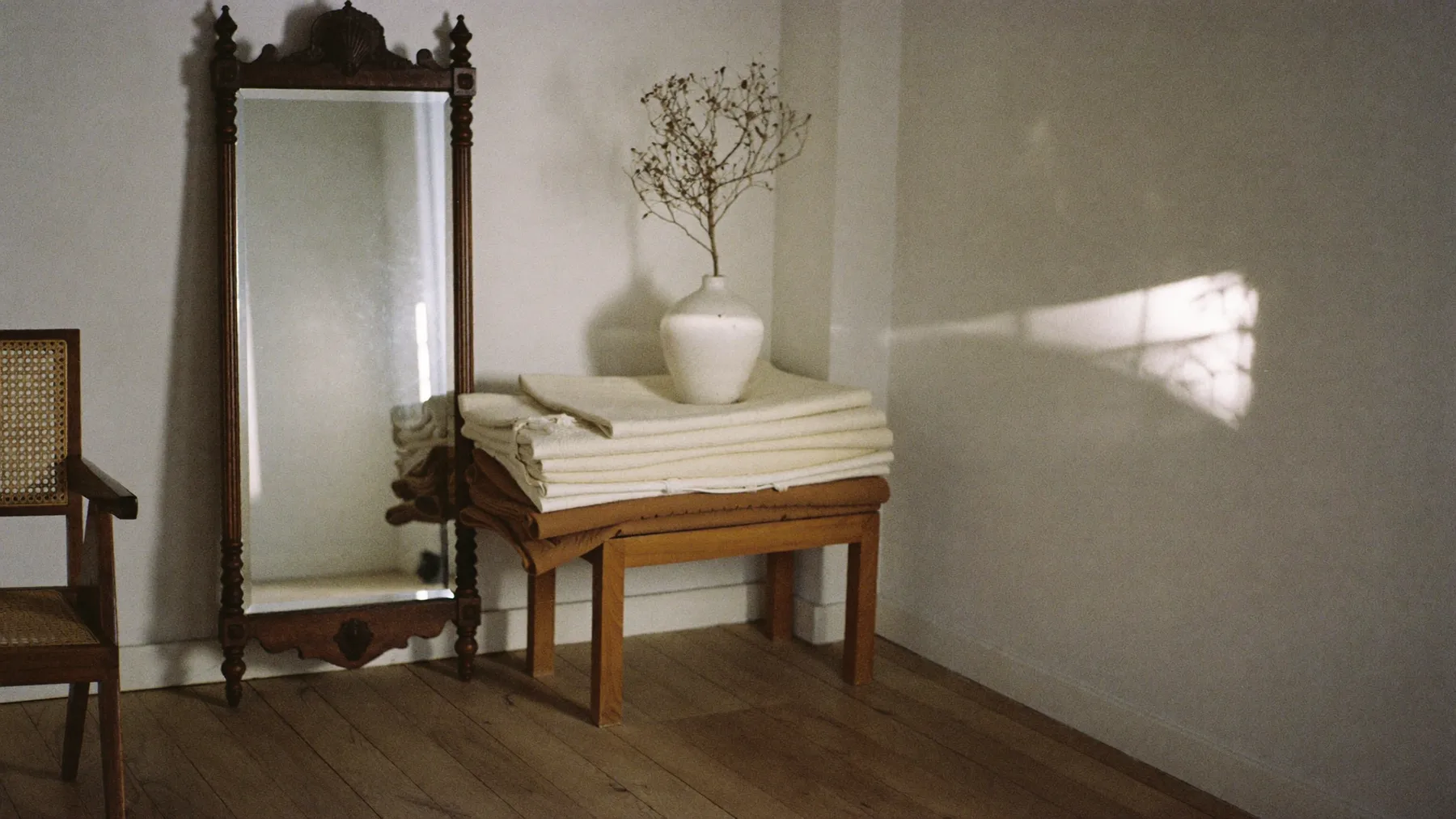 Coin du studio : miroir ancien, chaise cannée et drapés pliés sur un tabouret