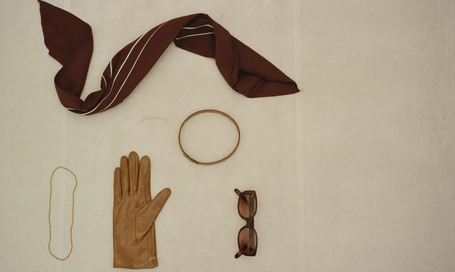 Foulard, ceinture, gants et lunettes disposés sur un lin écru